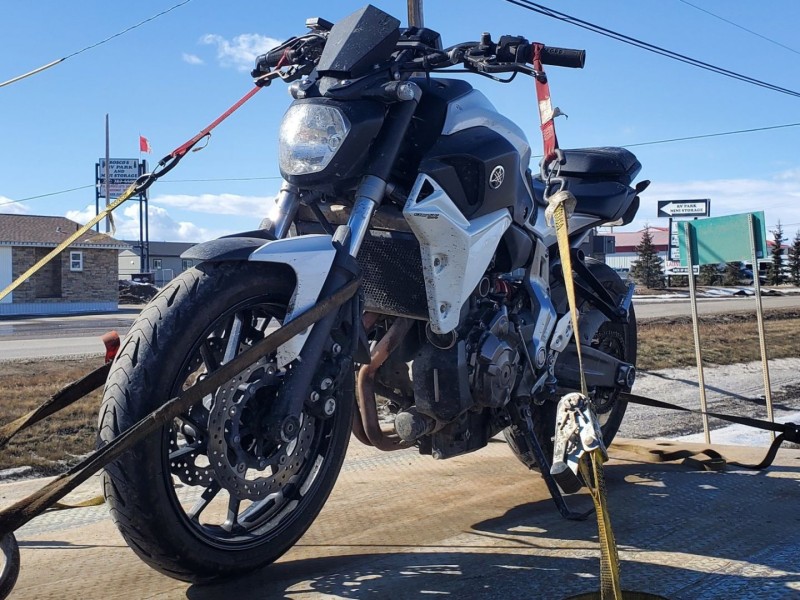 A motorcycle strapped to a tow truck bed on the roadside with buildings and signs in the background.