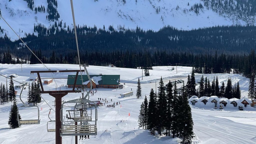 A photo taken from a ski lift heading towards a cabin with everything covered in snow. Trees in front of a hill in the background.