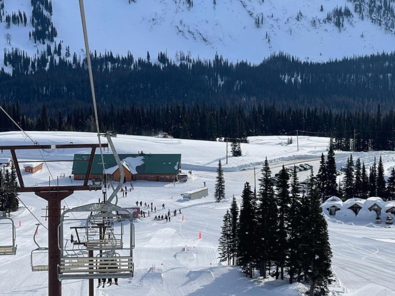 A photo taken from a ski lift heading towards a cabin with everything covered in snow. Trees in front of a hill in the background.
