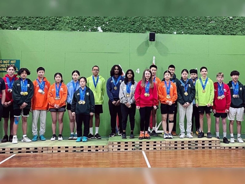 A large group of kids standing on platforms with medals around their necks in what appears to be a school gym.