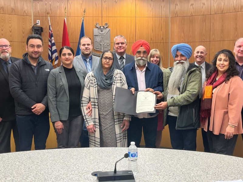A group of people stand in a wood paneled room posing for the camera around a proclamation.