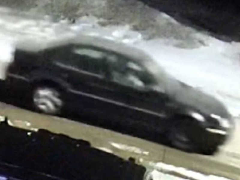 A shot from a security camera of a dark Volkswagen Jetta driving down a snowy street.