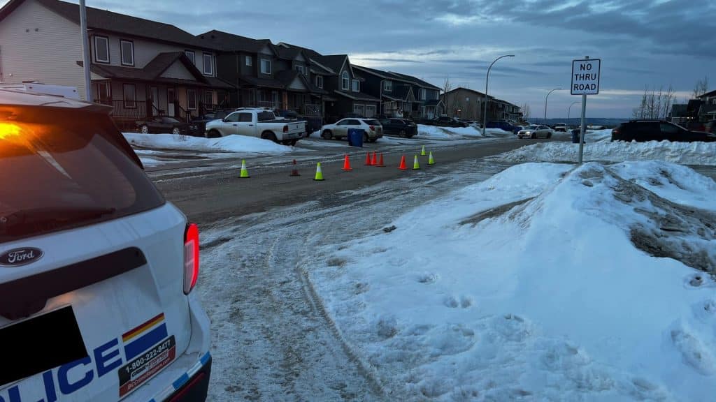 A suburban street in the early morning. A police car on the left and cones in the middle of the street block traffic.