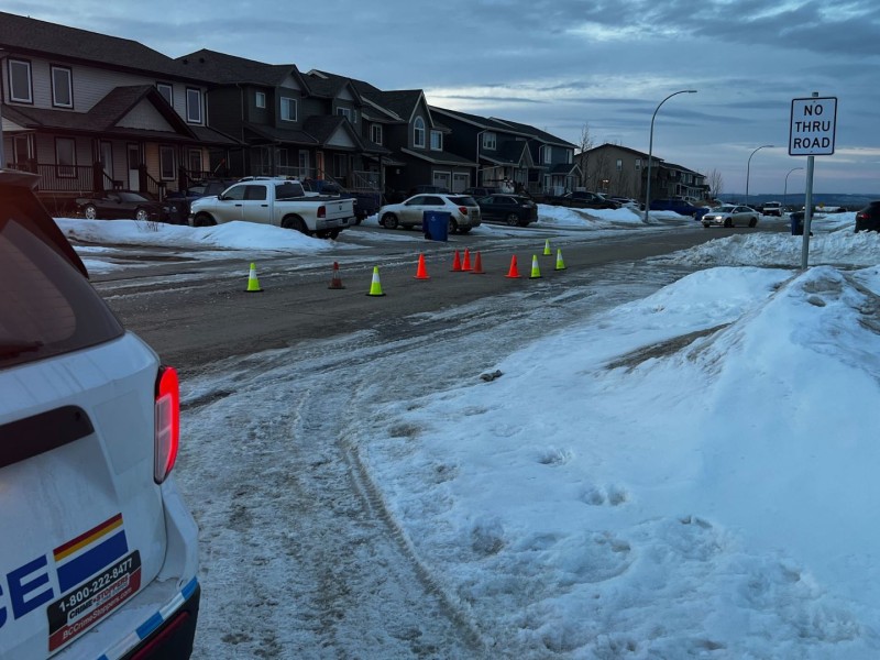 A suburban street in the early morning. A police car on the left and cones in the middle of the street block traffic.