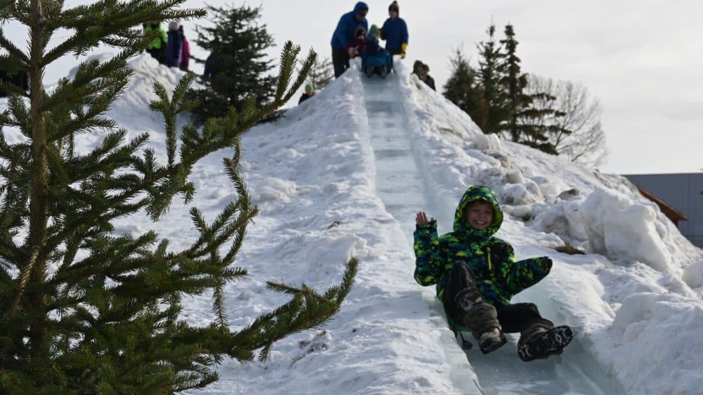 A child sliding down an ice slide with another child getting ready to slide down at the top.