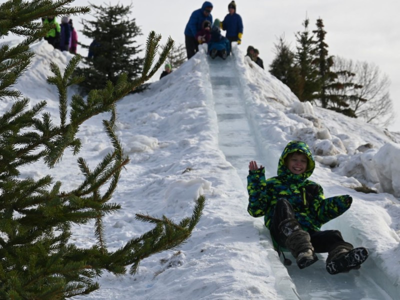 A child sliding down an ice slide with another child getting ready to slide down at the top.