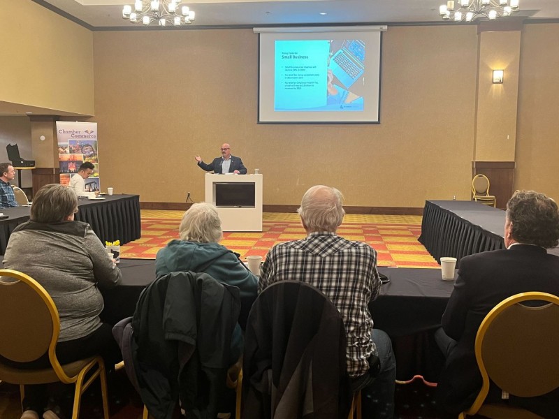 A room of people sit and watch a man in a suit speak at a podium.