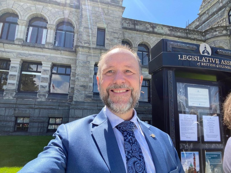 A late middle aged man in a blue suit with a grey beard.
