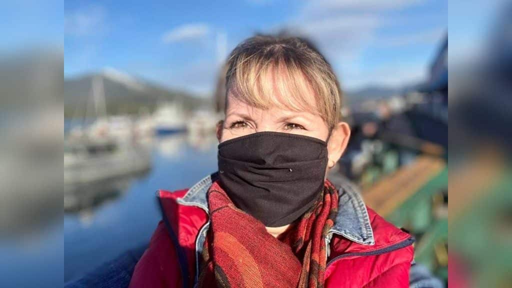 A photo of a lady next to water wearing a black mask, a red scarf and a red coat.