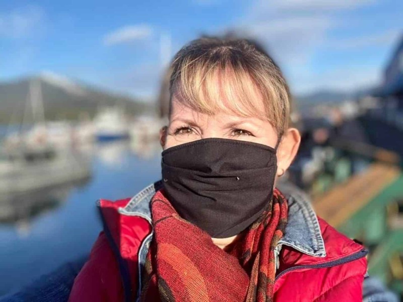 A photo of a lady next to water wearing a black mask, a red scarf and a red coat.
