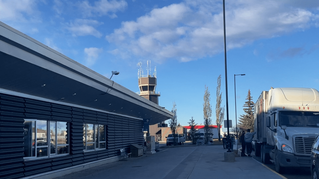 Outside an airport drop off area with a watch tower in the background and a larger truck on the right of the photo.