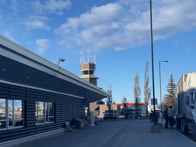 Outside an airport drop off area with a watch tower in the background and a larger truck on the right of the photo.