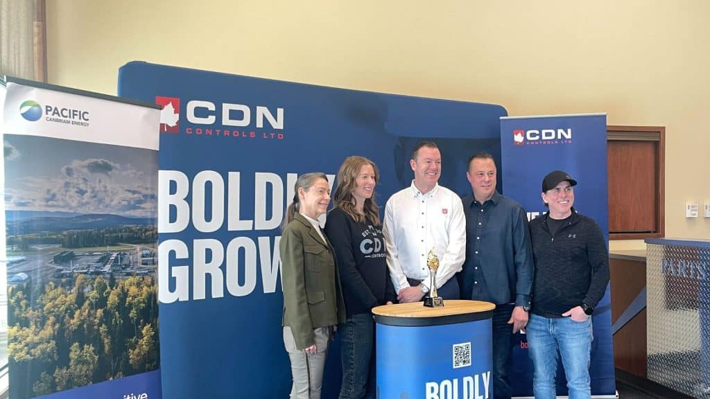 A line up of people in front of a CDN control banner, behind a podium with a small statue of a golden torch on it.