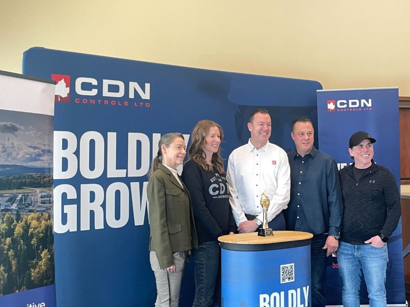 A line up of people in front of a CDN control banner, behind a podium with a small statue of a golden torch on it.