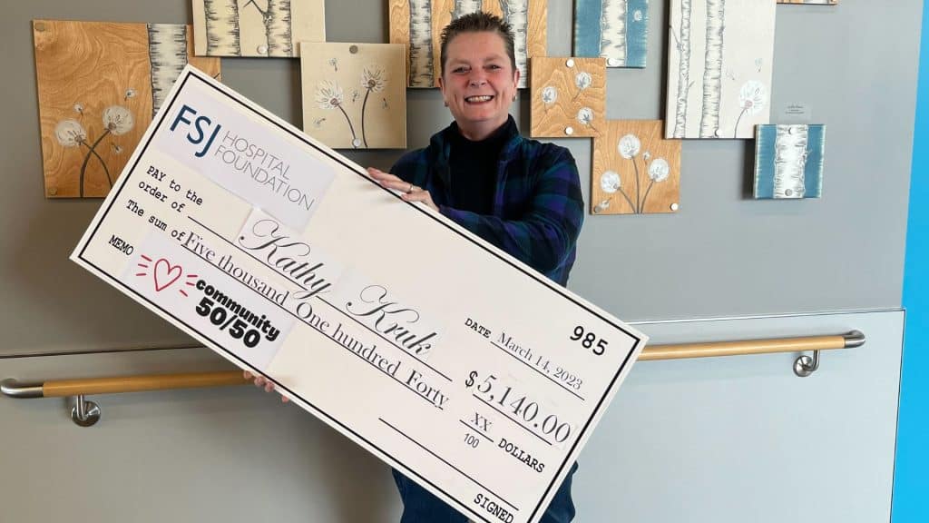 A late middle aged woman with short hair holds a large cheque for $5,140