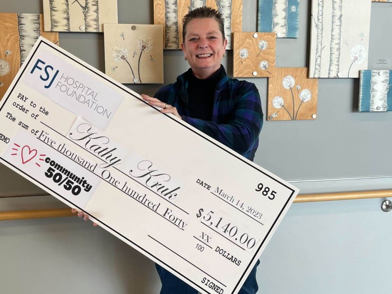 A late middle aged woman with short hair holds a large cheque for $5,140