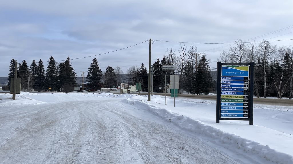 A road with a sign on the right hand side for directions around a town called Hudson's Hope.