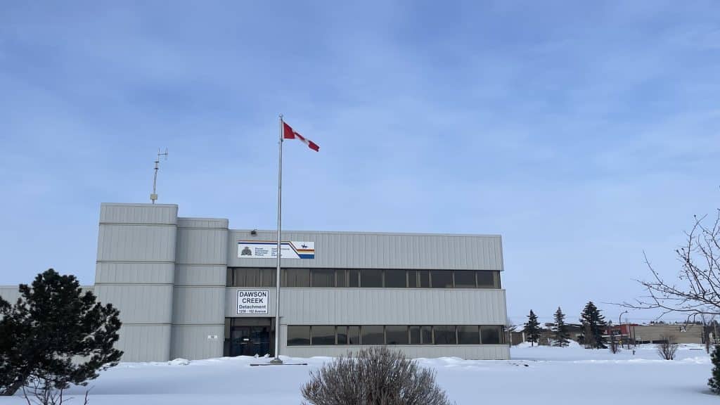 A grey building for the Dawson Creek RCMP detachment with a Canadian Flag in front.