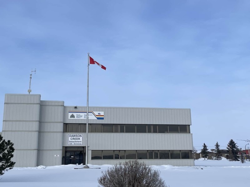 A grey building for the Dawson Creek RCMP detachment with a Canadian Flag in front.