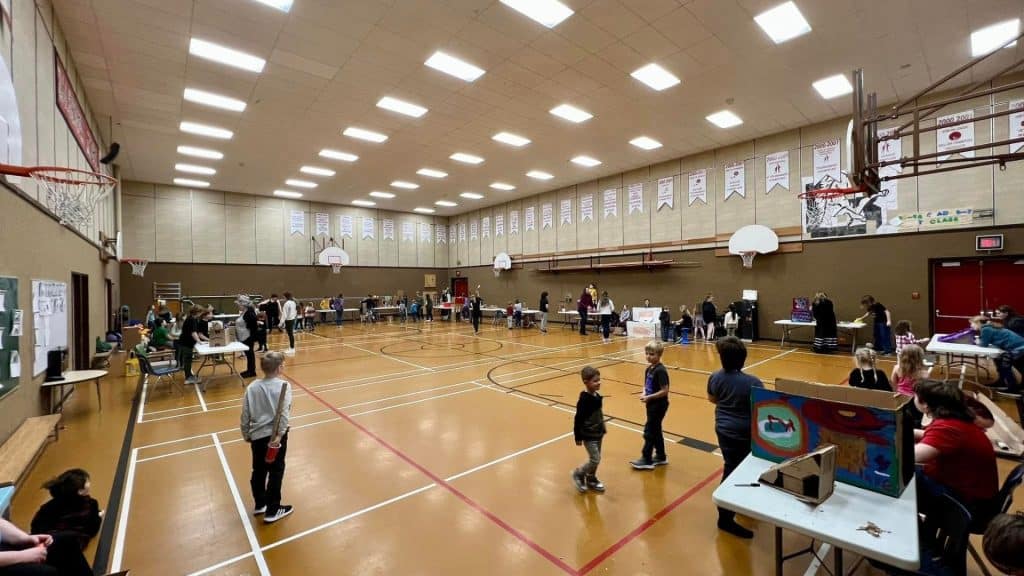 A school gymnasium with a bunch of students and tables for the cardboard arcade.