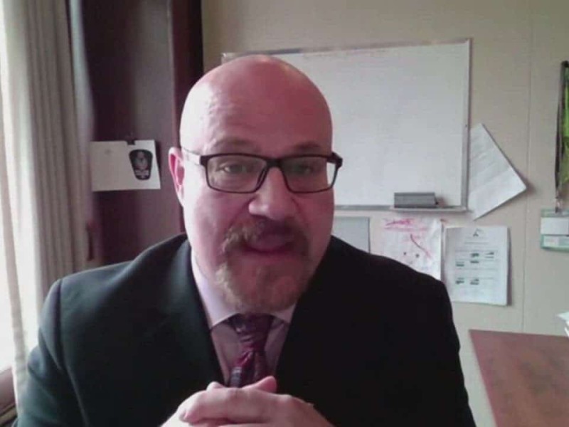 Person sitting in front of white board with hands clasped