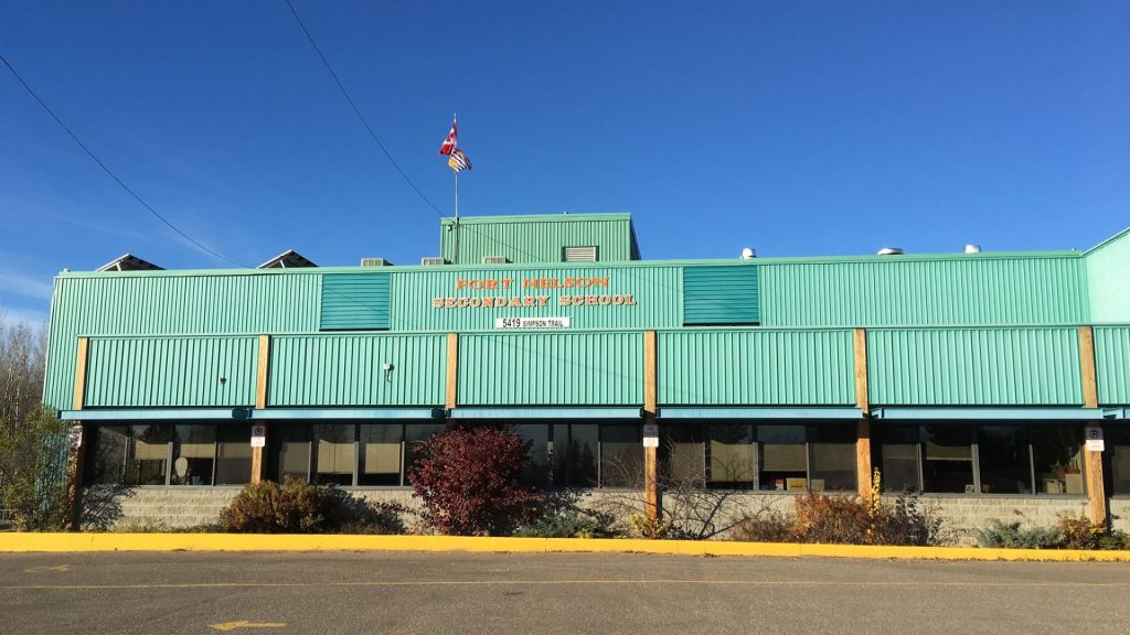 A blue building and parking lot. "Fort Nelson Secondary School" with the BC and Canadian flags.