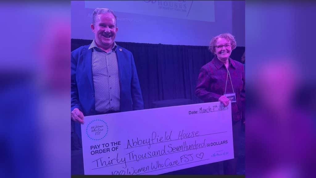 A man and a women each holding the sides of a large cheque for Abbeyfield house for the amount of thirty thousand, seven hundred dollars from the 100 Women Who Care FSJ.