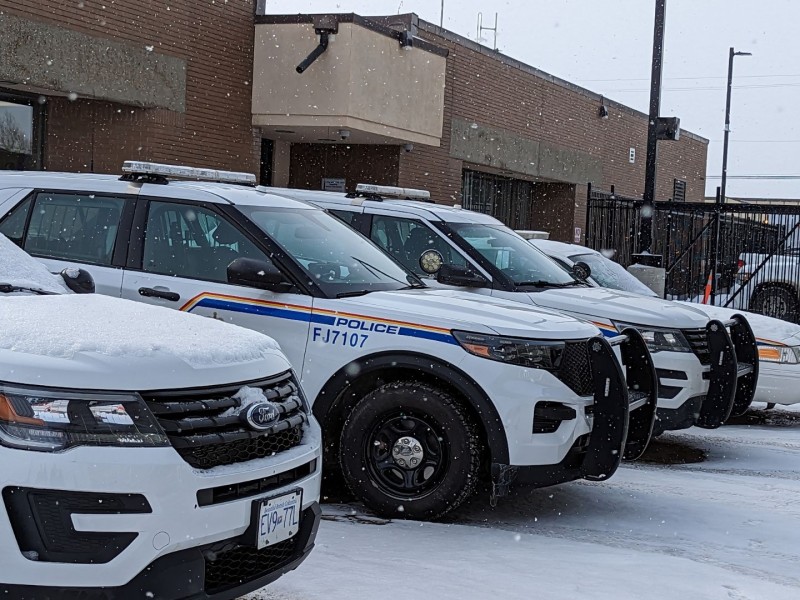A line of RCMP cruisers in front of a brick building.