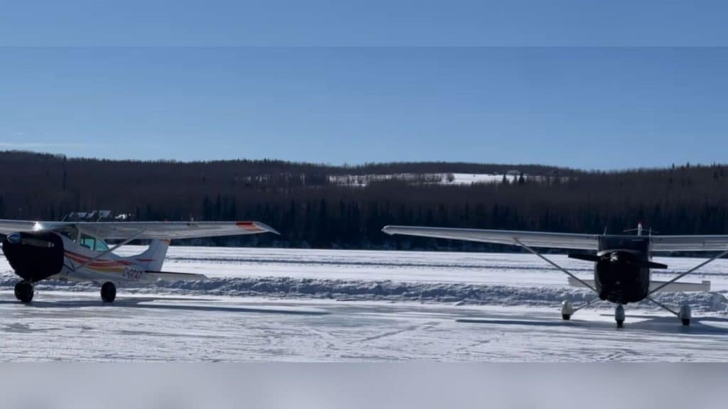 Two bush planes on a frozen lake with a forest in the background.