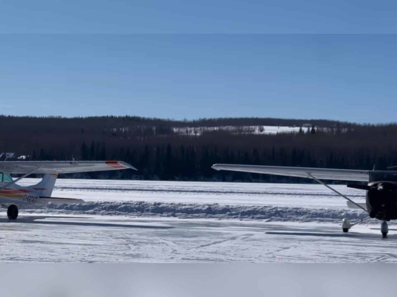 Two bush planes on a frozen lake with a forest in the background.
