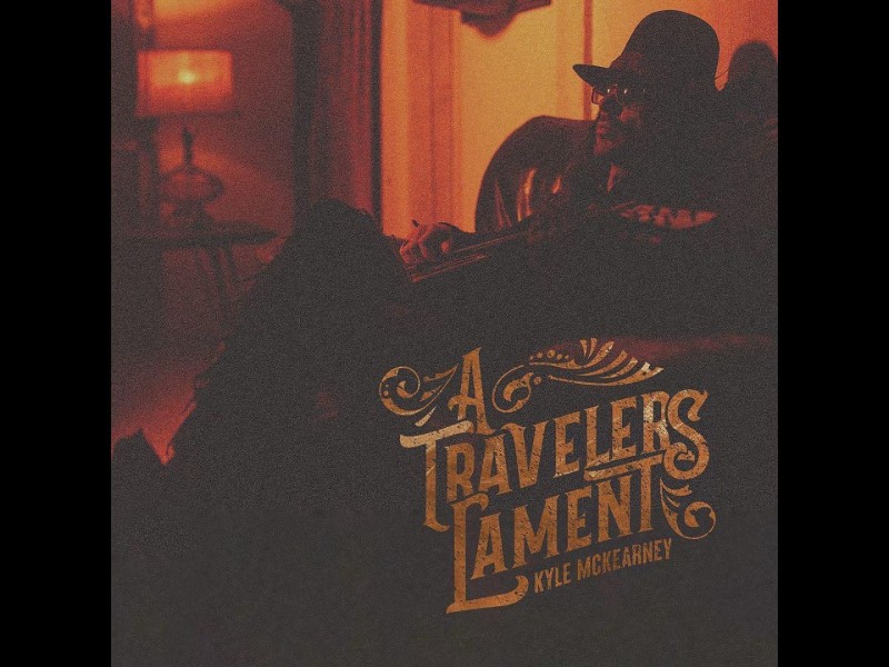 A grainy filtered photo of a man in a hat and sunglasses leaning back in a chair holding a guitar. The words "A Travelers Lament Kyle McKearney" are also in the photo.