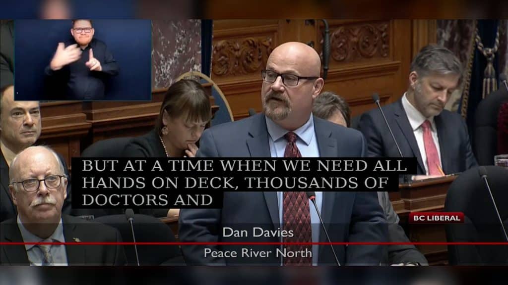 Dan Davies in a suit stands in the BC Legislature.