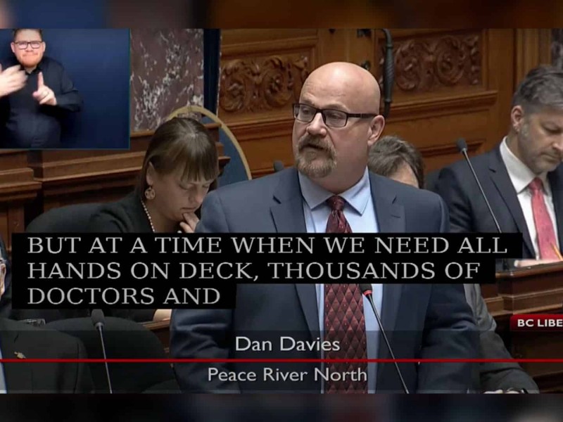 Dan Davies in a suit stands in the BC Legislature.