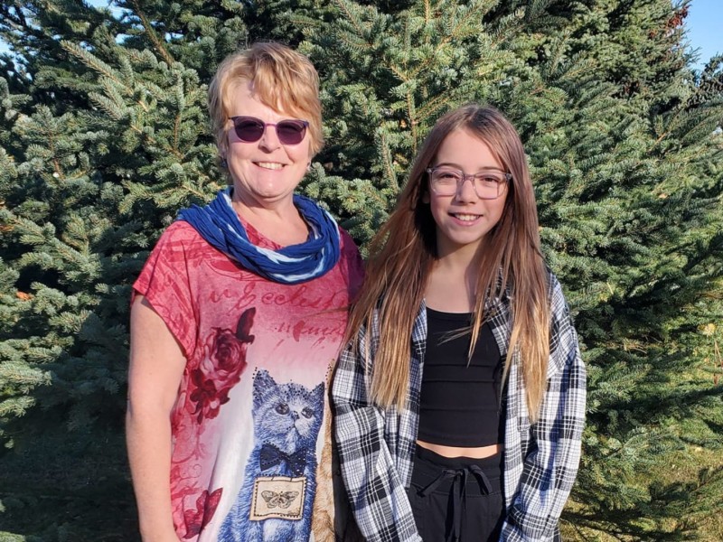 A woman and young girl standing in front of an evergreen tree.