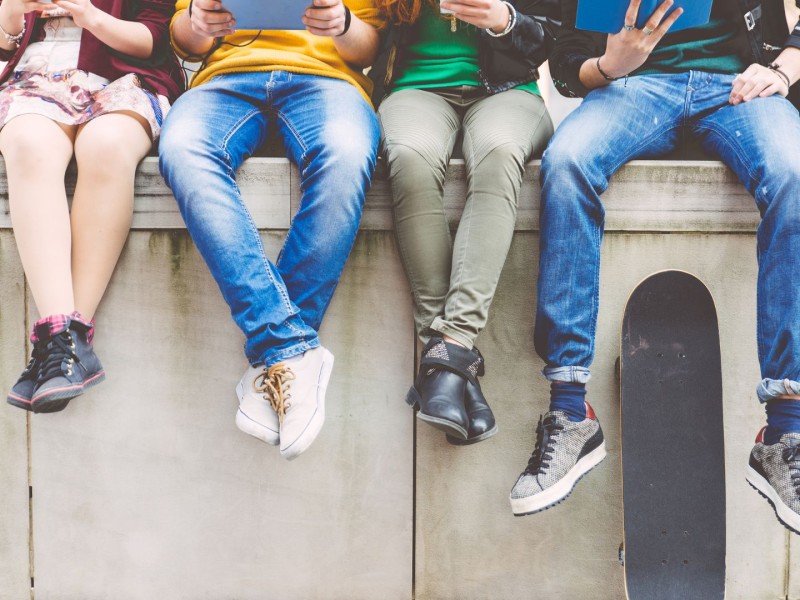 A group of teenagers sit together on a concrete wall.
