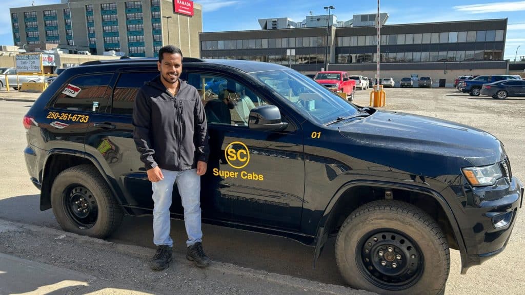 A man standing in front of a dark coloured taxi.