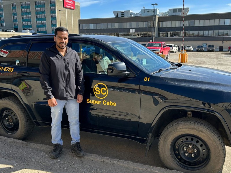 A man standing in front of a dark coloured taxi.