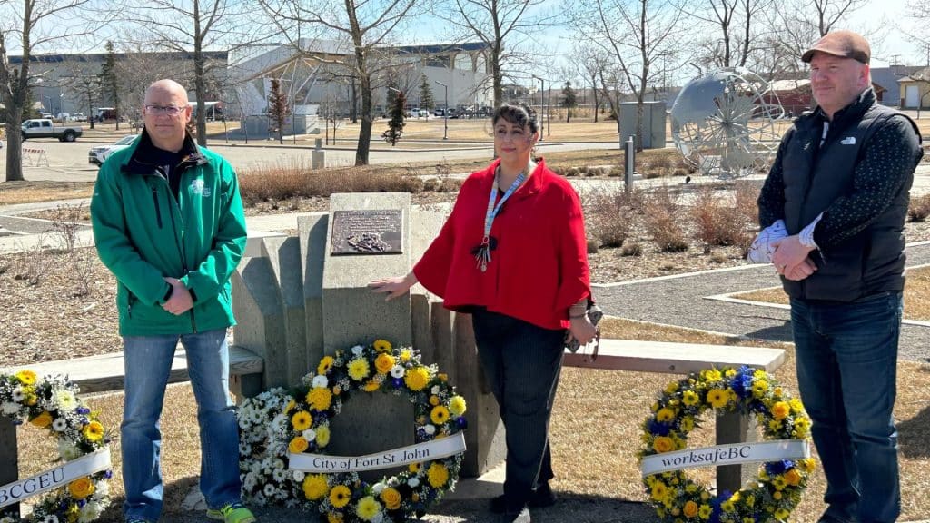 Three people standing beside the worker's memorial in Fort St. John with wreaths laid next to it.