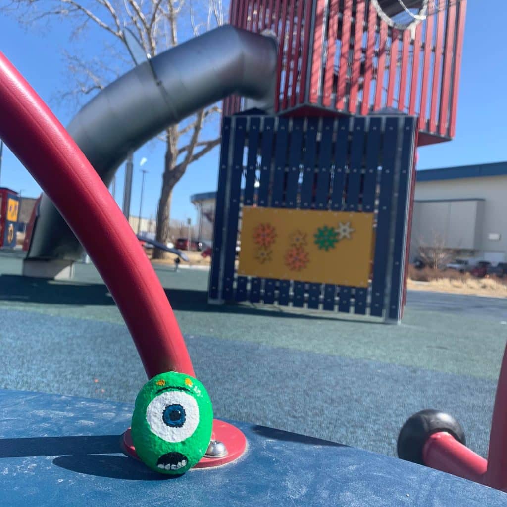 A rock painted like Mike from Monster's Inc sitting in a playground.