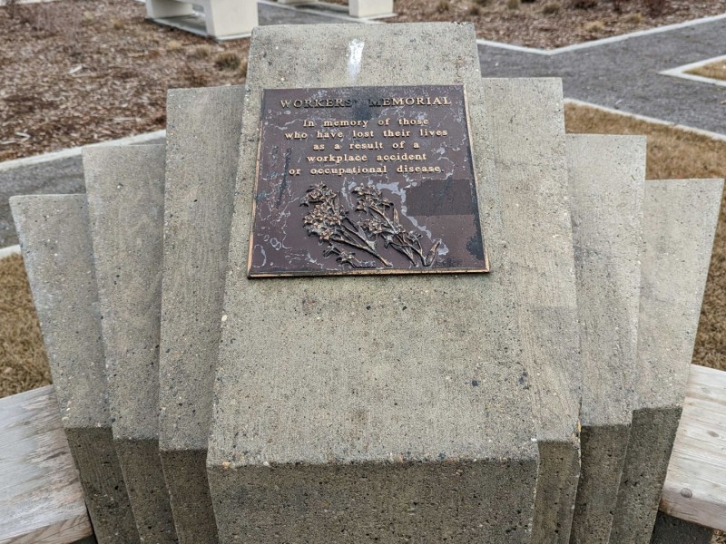 A Workers Memorial in Fort St. John in front of a parking lot full of cars. The plaque reads "Workers Memorial. In memory of those who have lost their lives as a result of a workplace accident or occupational disease."