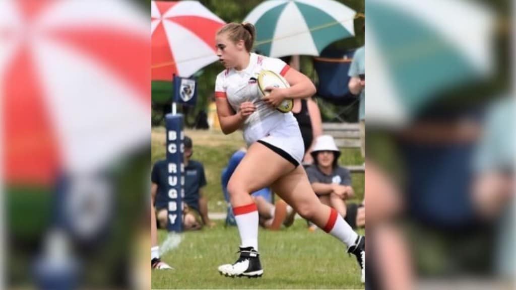 A picture of a girl in a white uniform and a pony tail running with a rugby ball.