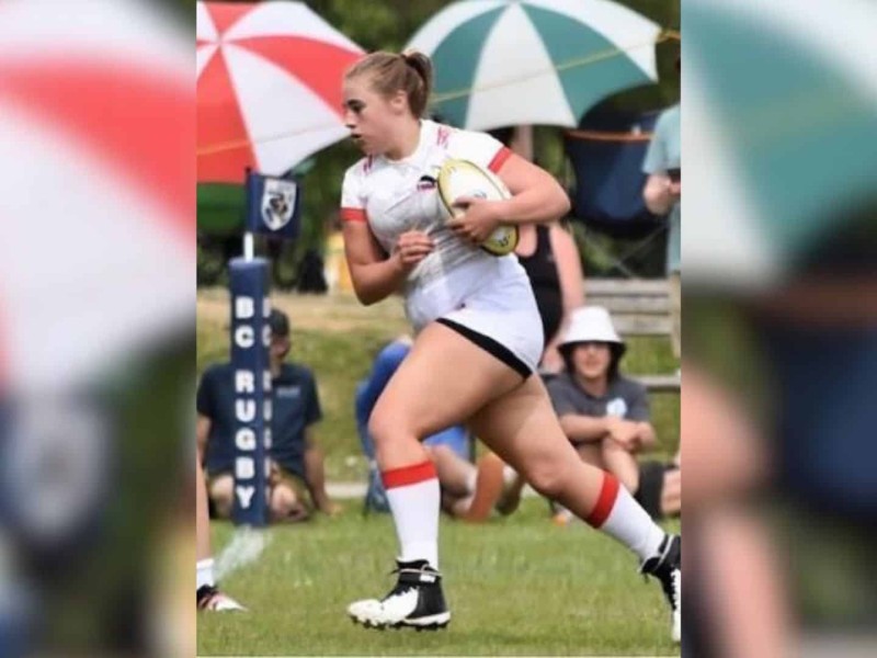 A picture of a girl in a white uniform and a pony tail running with a rugby ball.