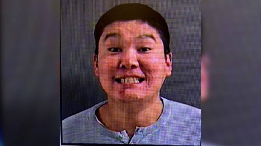 A man with dark hair smiling with his teeth on a grey background.