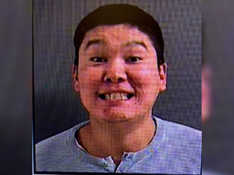 A man with dark hair smiling with his teeth on a grey background.