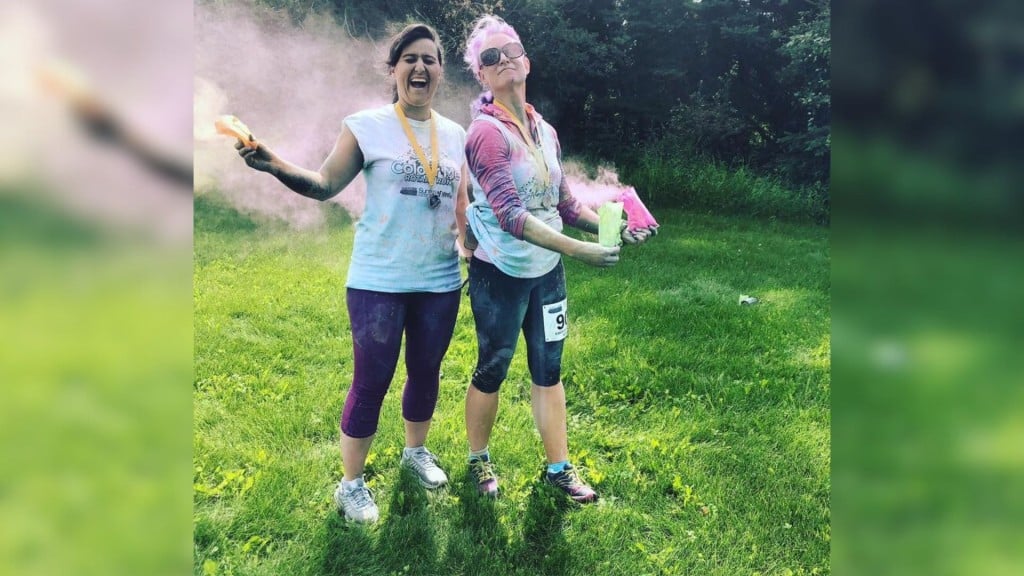Two women in running attire covered in green and pink pigment.