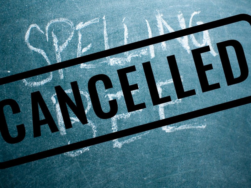 "Spelling Bee" written in white on a green chalkboard, with black writing saying "Cancelled" over top of it.