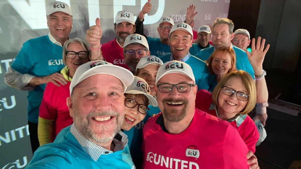 A group of people in white hats, and pink and teal shirts that read BC United.