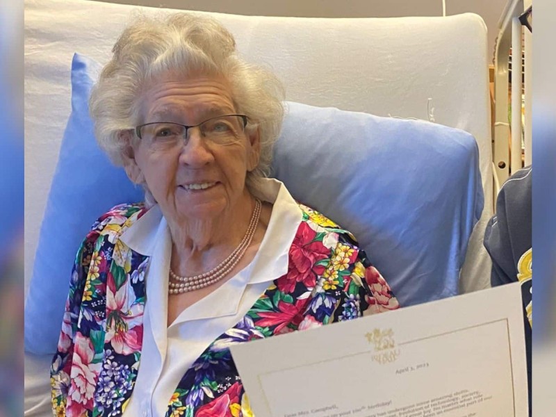 A white haired older woman sitting up in a bed.