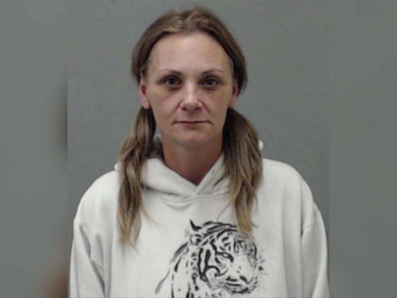 A woman in a white hoodie with a tiger on it standing in front of a grey wall.