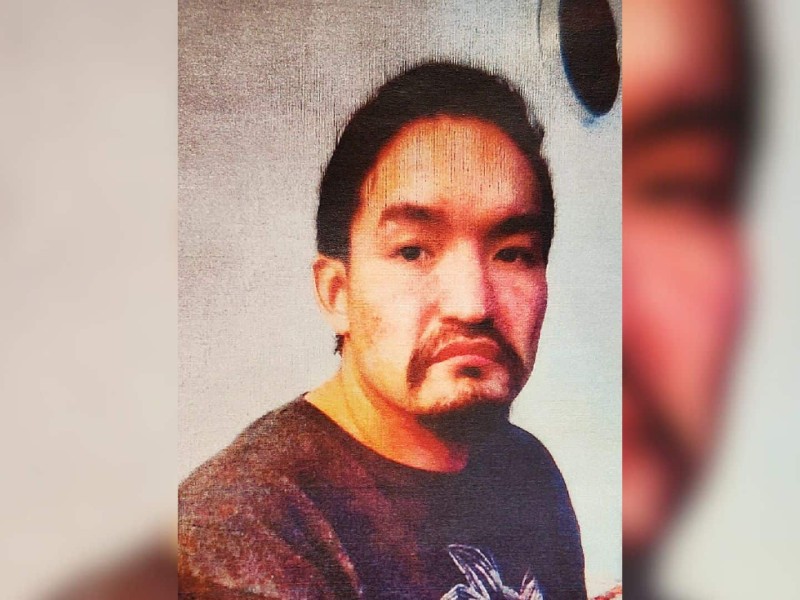 A man with dark hair, dark eyes and a black beard and mustache wearing a brown shirt.